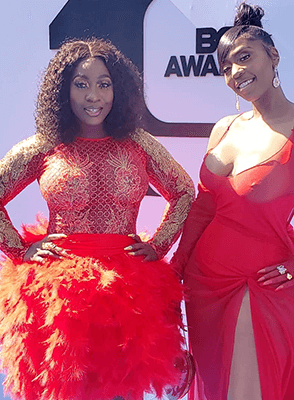 Dancehall artist Spice and a young lady wearing matching red dresses, posing together.
